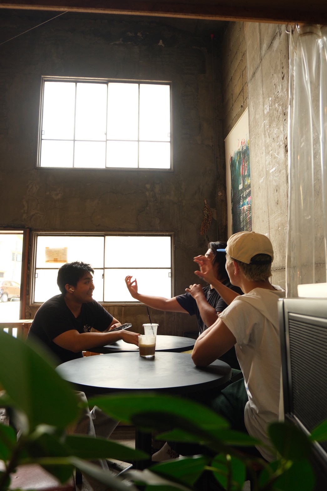TUMUGU COFFEE STANDの高い天井の店内で、テーブルを囲んで会話を楽しむお客さまたち
